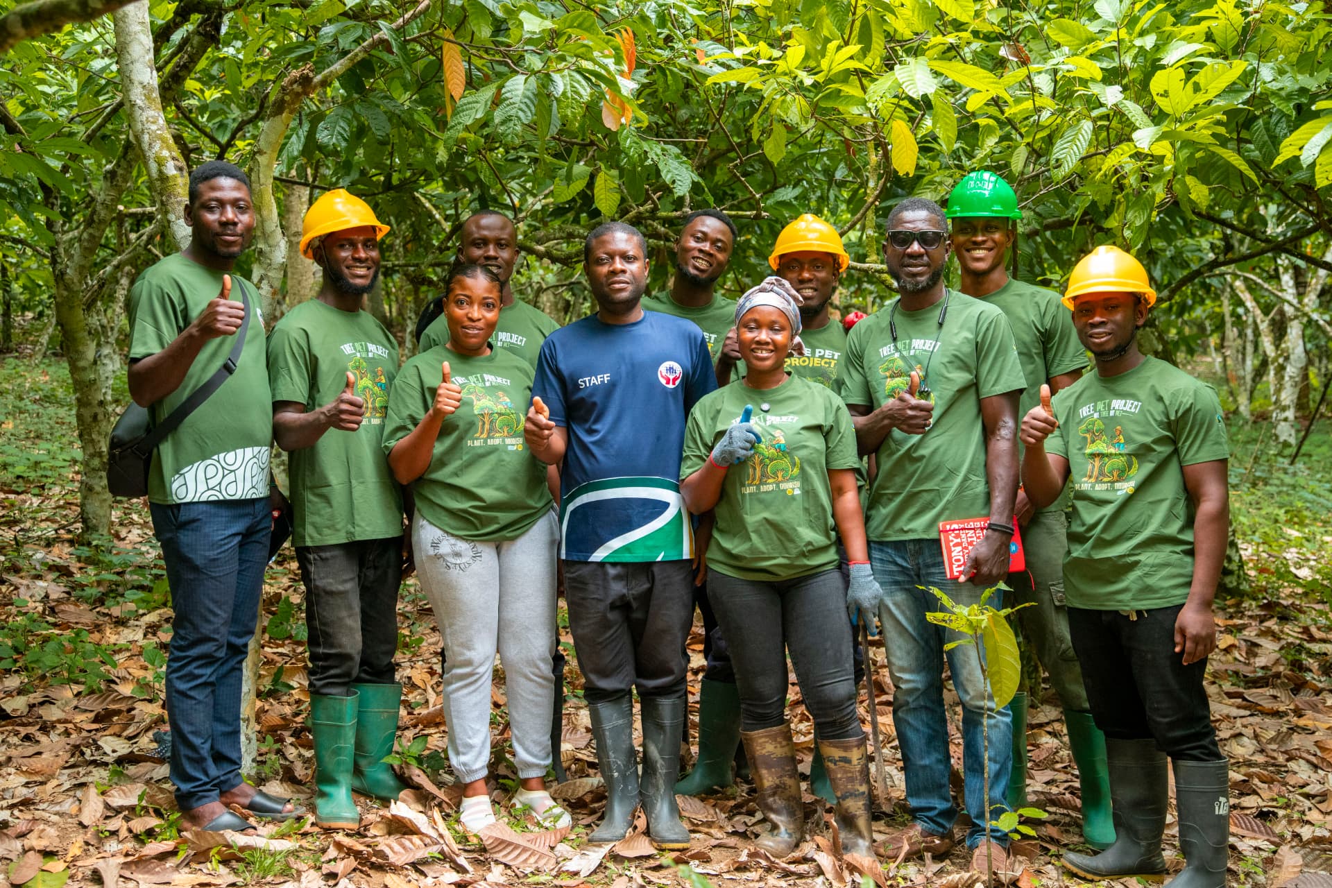 Asetenapa staff and members in Tree PET Project shirts standing among cocoa trees with a seedling